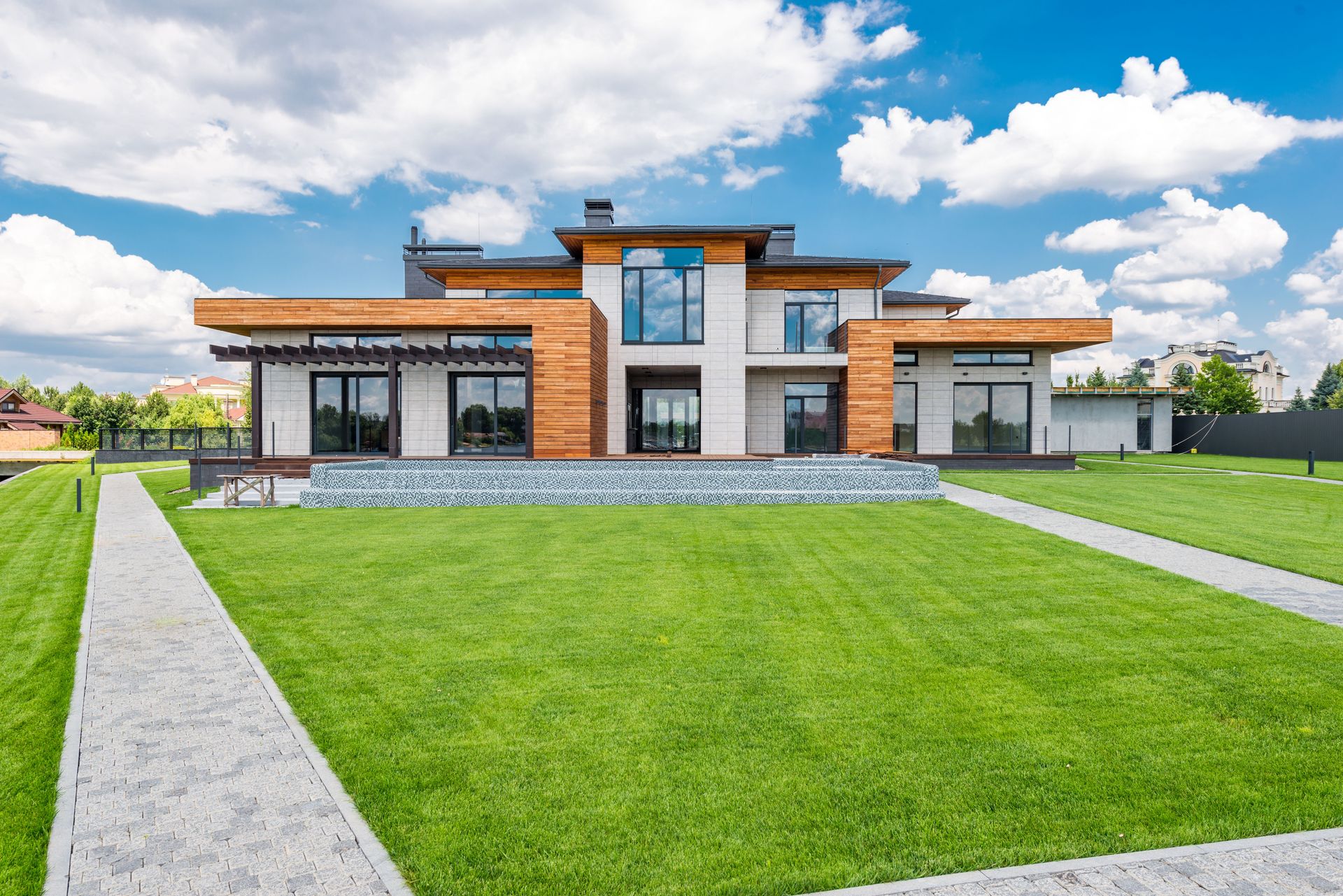 Exterior of contemporary residential house with glass doors and panoramic windows near green lawn with paved paths on sunny day in summer